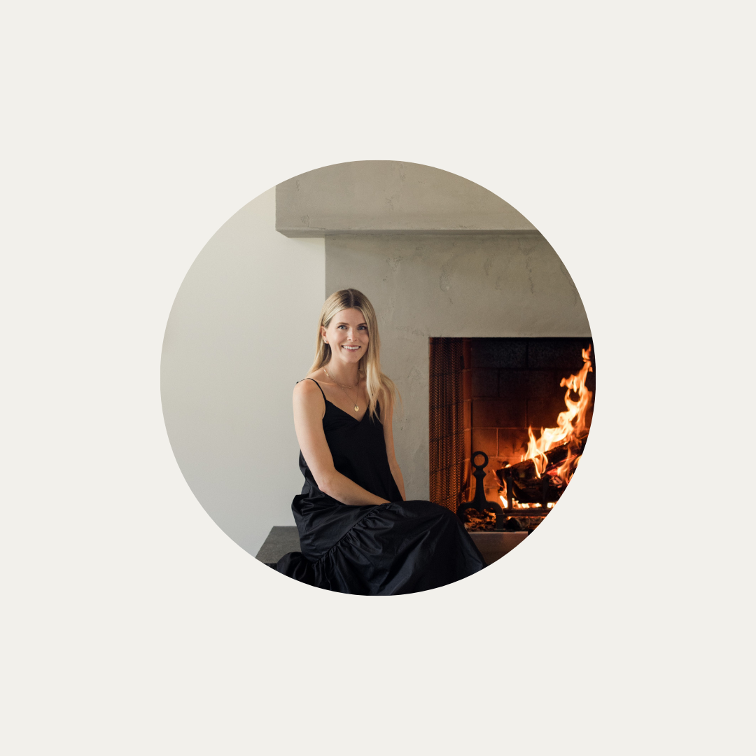 A woman sitting beside a cozy fireplace.