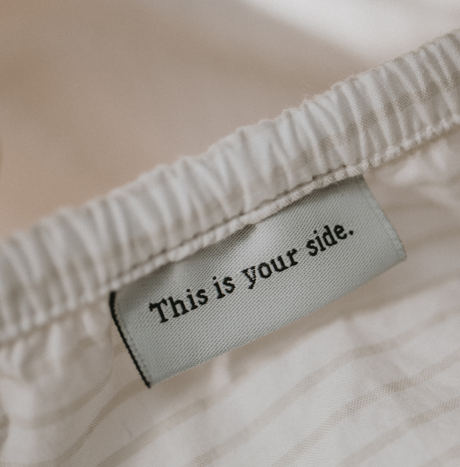 Close up of Tuck's crisp pinstriped pillowcase. A tag reads, "This is your side."
