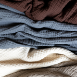 Stack of textured fabric swatches in brown, blue, cream and beige.