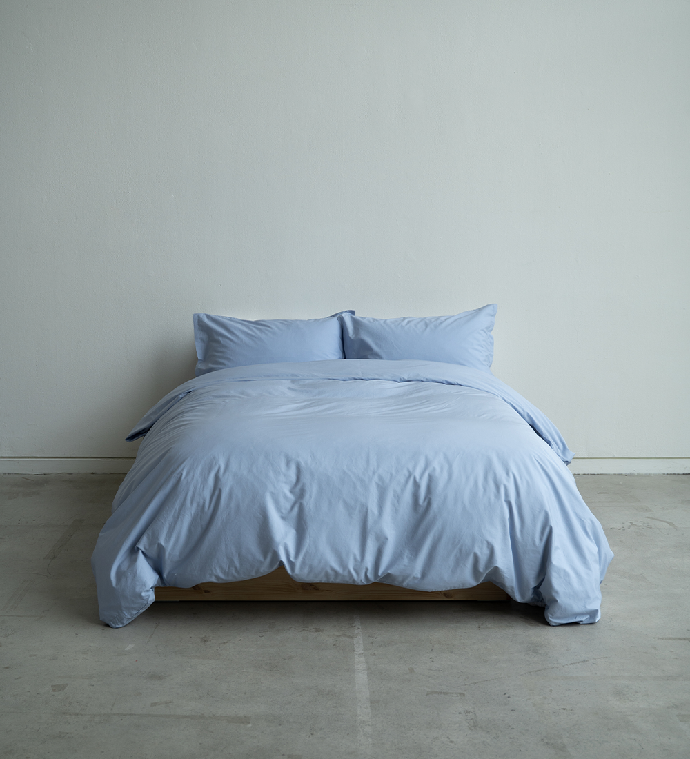 Blue bedding set on a bed against a plain wall.