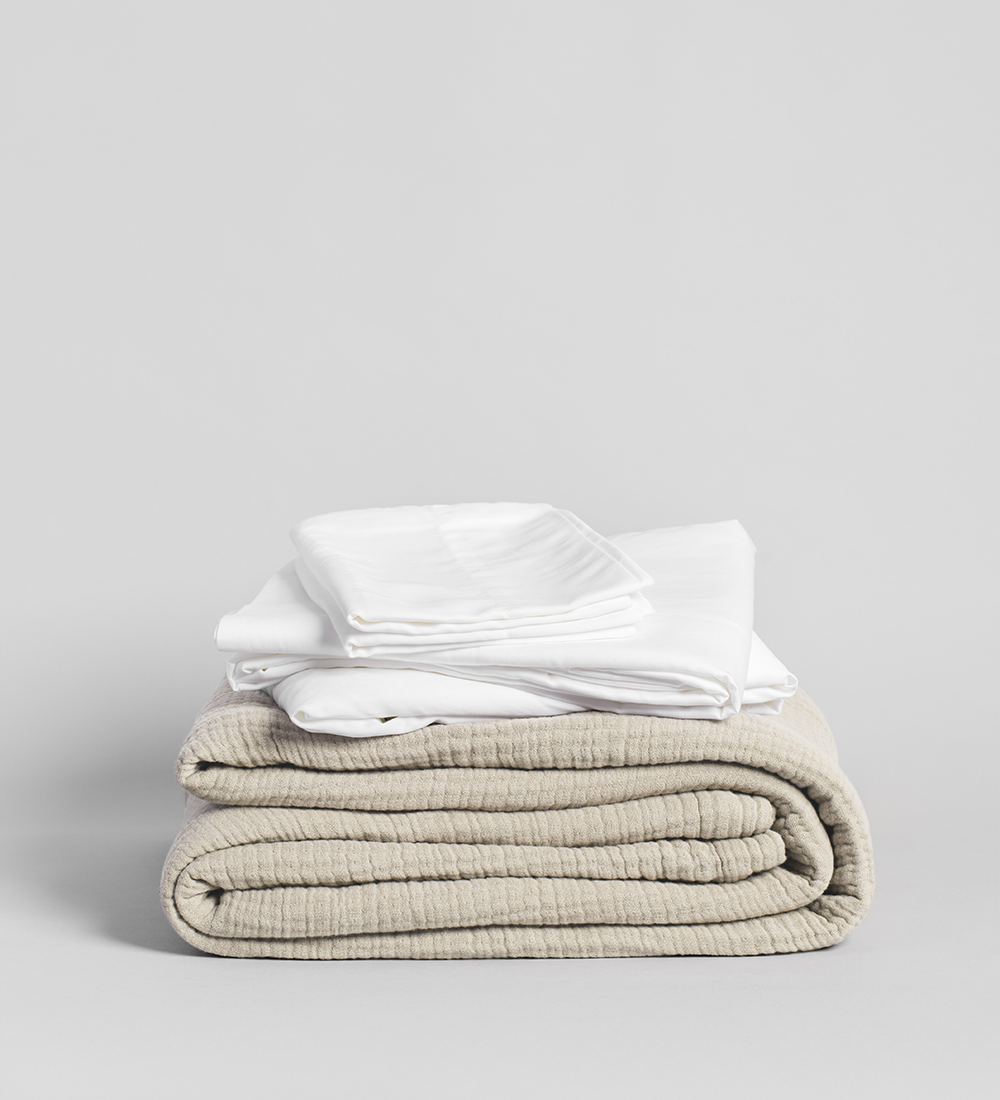 Stack of folded white shirts and a cream blanket on a light gray background
