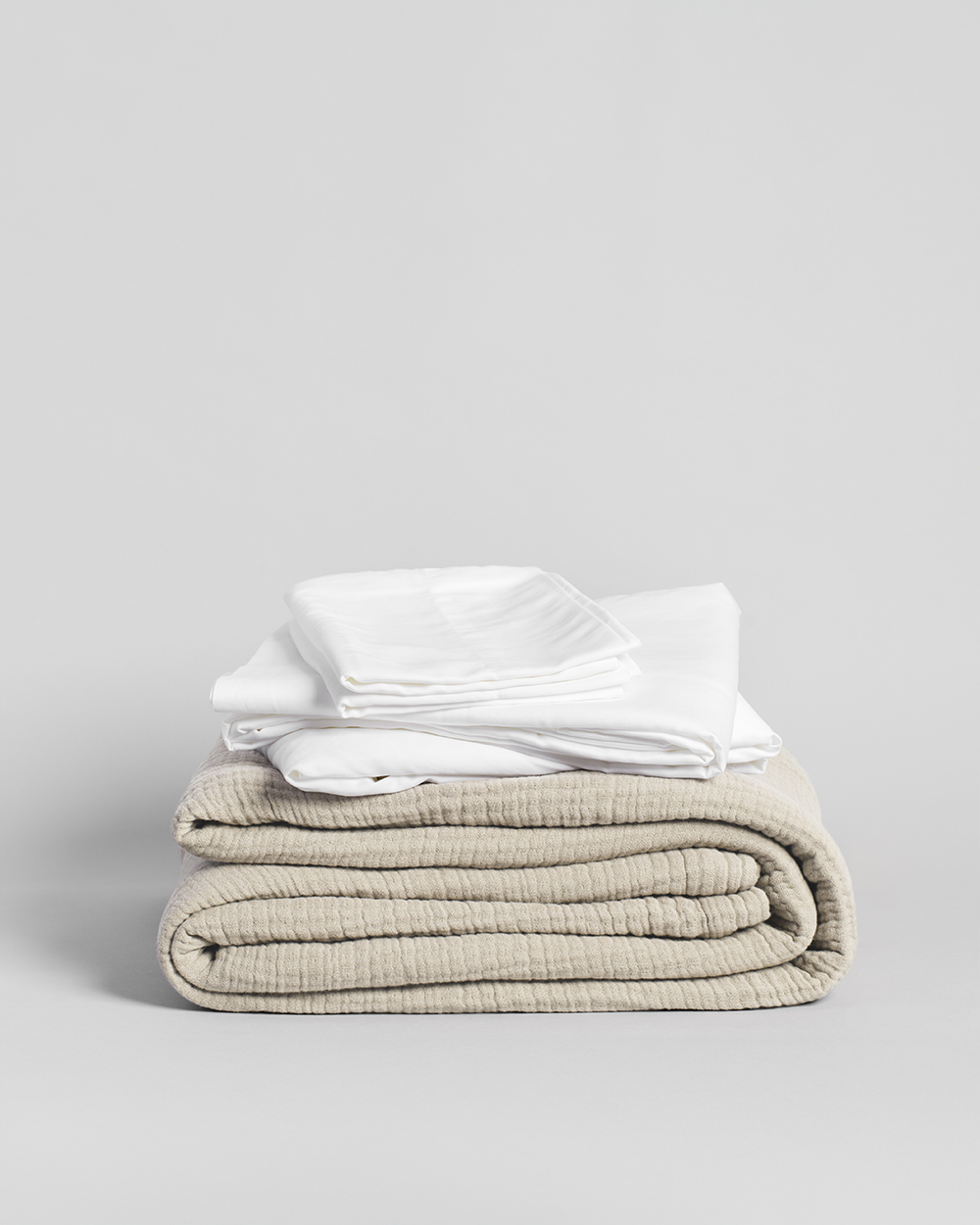 Stack of folded white shirts and a cream blanket on a light gray background