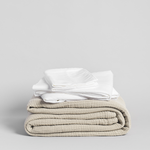 Stack of folded white shirts and a cream blanket on a light gray background