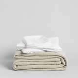 Stack of folded white shirts and a cream blanket on a light gray background